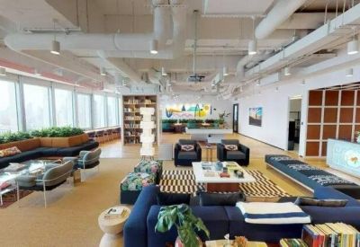 Spacious open-plan communal hub featuring blue sofas, a striped rug, and exposed ceiling pipes.