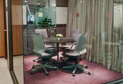 Small glass-walled meeting room with a round table and grey ergonomic chairs.