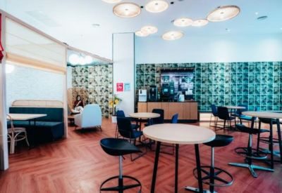 Bright communal lounge and cafe area with patterned wallpaper, various seating options, and warm wooden flooring.