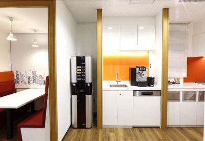 Modern communal kitchen area featuring a coffee machine, white cabinetry, and orange backsplash.