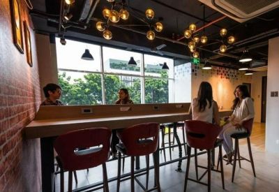 Spacious coworking lounge with warm pendant lighting, wooden bar seating, and a large window view.