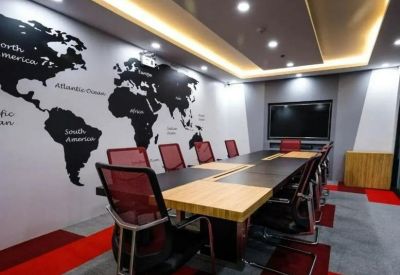Bright boardroom featuring a large world map mural, wooden conference table, and red mesh chairs.