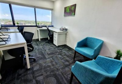 Private office with two white desks and blue armchairs overlooking a city view.