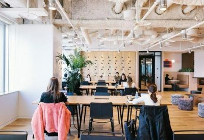 Bright open-plan workspace featuring long communal desks and large windows.