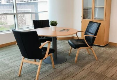 Small meeting area with a round wooden table and three black leather chairs.