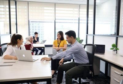 Open-plan office area with team members working at white desks near large windows.