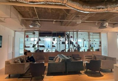 Modern coworking lounge featuring a glass-partitioned bookshelf wall and grey fabric sofas.