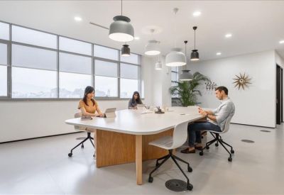 Modern coworking space with a large wooden table, designer pendant lights, and indoor plants.