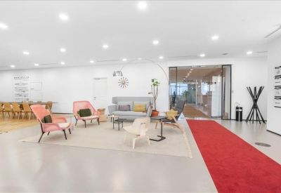Modern reception lounge with pink armchairs and a long red carpet leading to glass doors.