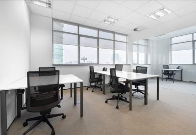 Bright open-plan office with white desks and black ergonomic chairs near large windows.