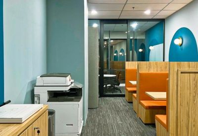 Office corridor featuring orange semi-private work booths and a printer station.