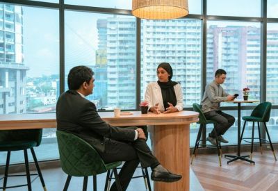 Meeting area with green chairs and floor-to-ceiling windows offering city views.