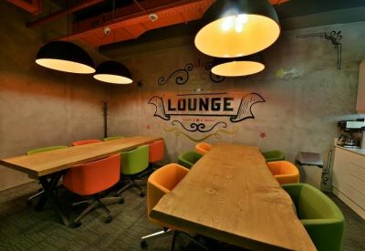 Bright breakout area featuring natural wood tables and vibrant orange and green chairs.