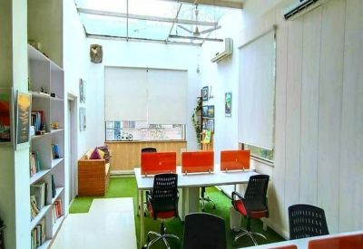 Bright, sunlit office with white desks, orange privacy screens, and artificial grass flooring.