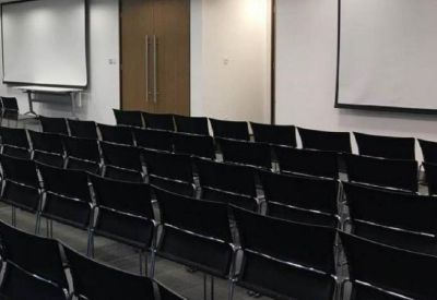 Large presentation room with multiple rows of black chairs facing two large white projector screens.