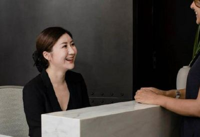 Close-up of a smiling receptionist at a marble front desk assisting a visitor.