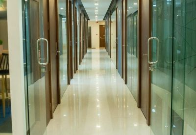 Brightly lit office corridor with glass doors and polished white flooring.