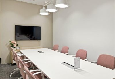 Meeting room with a long white table, pink chairs, and a large wall-mounted monitor.