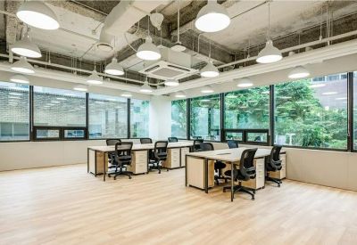 Open-plan office with wooden desks and ergonomic black chairs by large windows.
