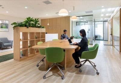 Communal coworking space with green armchairs and a central wooden table with plants.