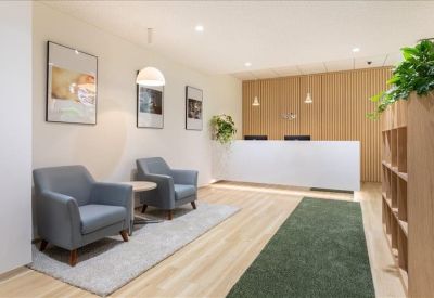 Reception lobby featuring grey armchairs, a white front desk, and wooden wall panels.