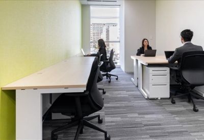 Bright, open-plan office space with long wooden desks and ergonomic black chairs.