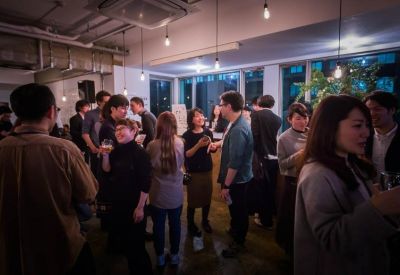 Crowded communal lounge area with people networking under hanging light bulbs.