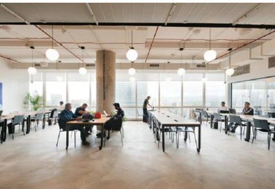 Bright open-plan coworking area with long white desks and views through large windows.