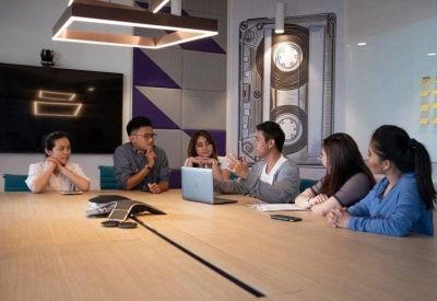 Team meeting around a light wood conference table in a room with a large cassette tape mural.