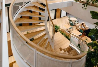Modern spiral staircase with wooden treads and white railings connecting office floors.