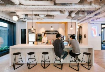 Modern office pantry with a long white breakfast bar and industrial-style exposed piping.