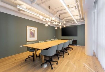 Meeting room with a long wooden table, grey ergonomic chairs, and a minimalist chandelier.