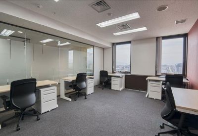 Bright shared office with several white desks and black ergonomic chairs.