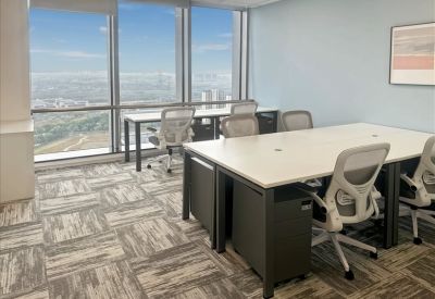 Professional open-plan workspace with multiple desks and floor-to-ceiling windows showing city views.