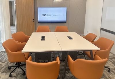 Modern conference room with a white table, ten orange chairs, and a large wall-mounted monitor.