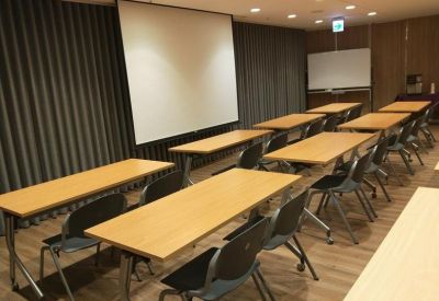 Training room set up with wooden tables, grey chairs, and a large projection screen.