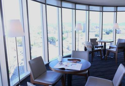 Bright corner lounge area with round tables and floor-to-ceiling city views.