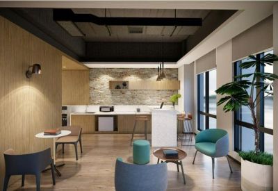 Bright breakout space with teal armchairs, a small kitchen, and a feature stone wall.
