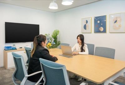 Meeting room with a large wooden table, blue chairs, and a wall-mounted screen.