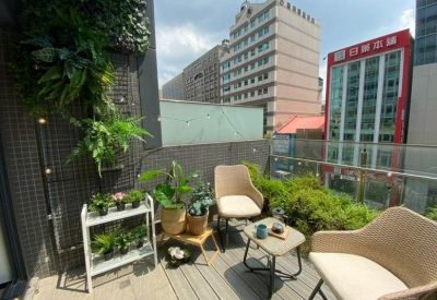 Sunny rooftop communal terrace with wicker armchairs, potted plants, and city building views.