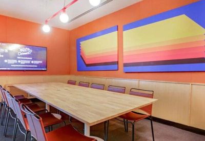 Vibrant meeting room with a long wooden table, orange chairs, and bold geometric wall art.