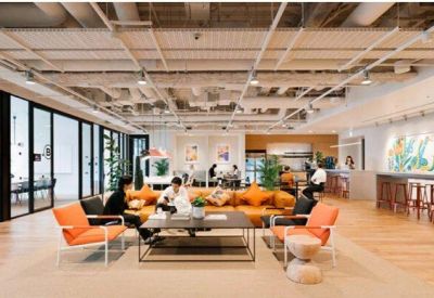 Bright coworking area with orange armchairs, large sofas, and expansive floor-to-ceiling windows.