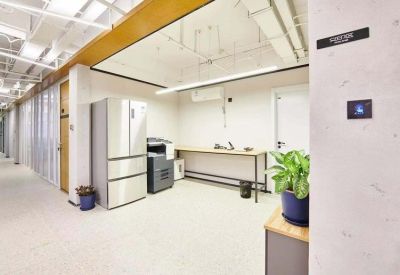 Communal kitchen area with a refrigerator, printer, and prep counter next to a potted plant.