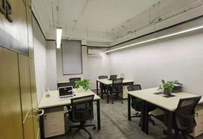 Modern four-person office suite with light-colored desks, green plants, and bright overhead lighting.
