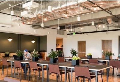 Large open-plan workspace featuring long wooden desks, indoor plants, and an industrial-style ceiling.