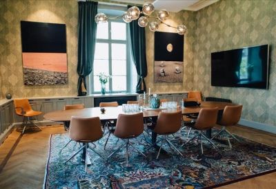 Meeting room with patterned wallpaper, large dining table, and a statement bubble chandelier.