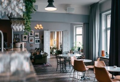 Bright breakout area with cafe tables, leather chairs, and large windows with grey curtains.