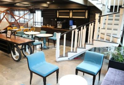 Reception lounge featuring blue armchairs, a wooden cart table, and a white spiral staircase.
