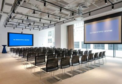 Large professional seminar room with rows of black mesh chairs and dual projection screens.