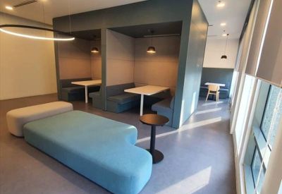 Modern communal breakout area featuring a blue curved sofa and private dining-style booths.